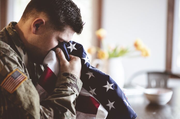 American soldier mourning and praying with the American flag in his hands