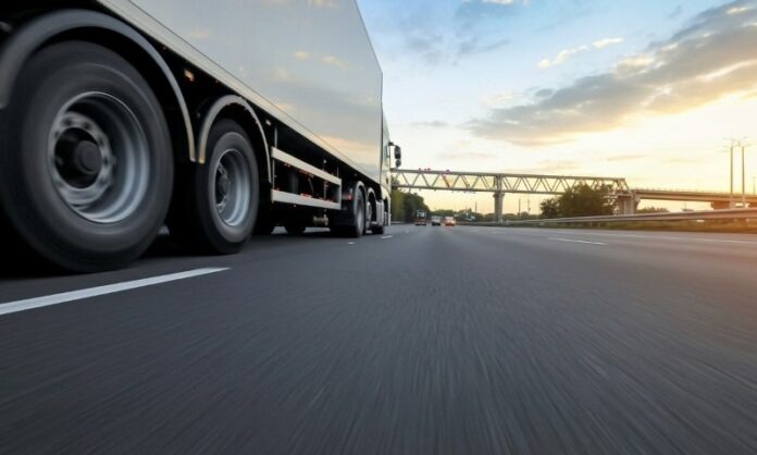 Large truck wheels blur past on a dark highway at sunrise