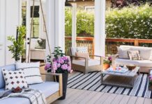 Stylish patio with light wood furniture, pastel cushions, potted flowers, and a black-striped rug