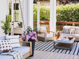 Stylish patio with light wood furniture, pastel cushions, potted flowers, and a black-striped rug