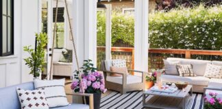 Stylish patio with light wood furniture, pastel cushions, potted flowers, and a black-striped rug