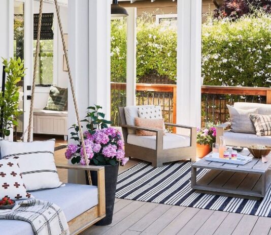 Stylish patio with light wood furniture, pastel cushions, potted flowers, and a black-striped rug
