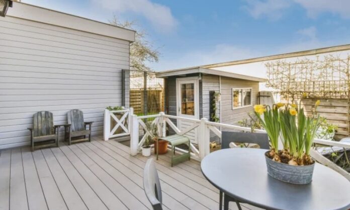 A modern patio features a round table with yellow flowers, surrounded by wooden chairs