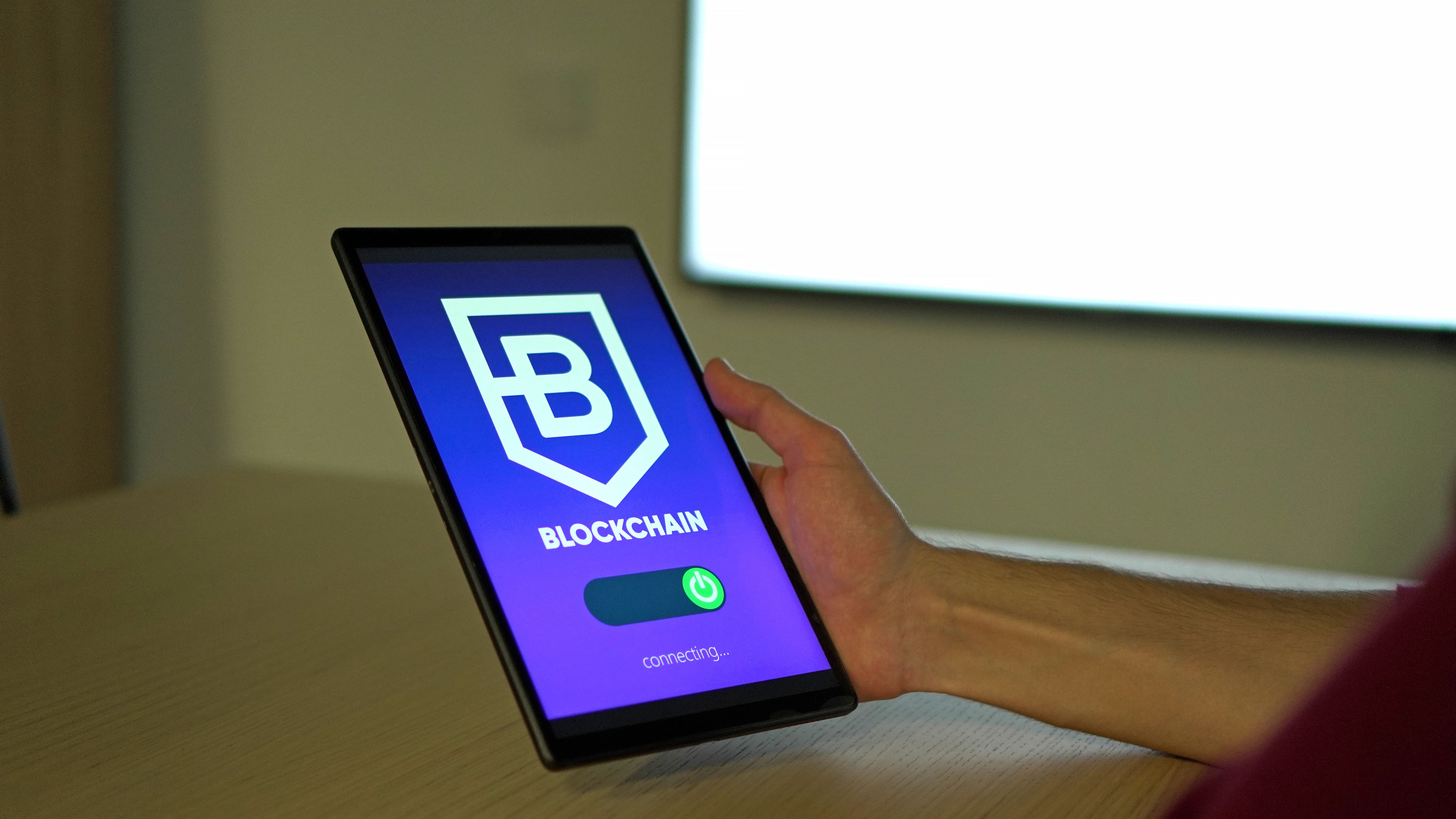 Hand holding a tablet displaying a blockchain logo on screen
