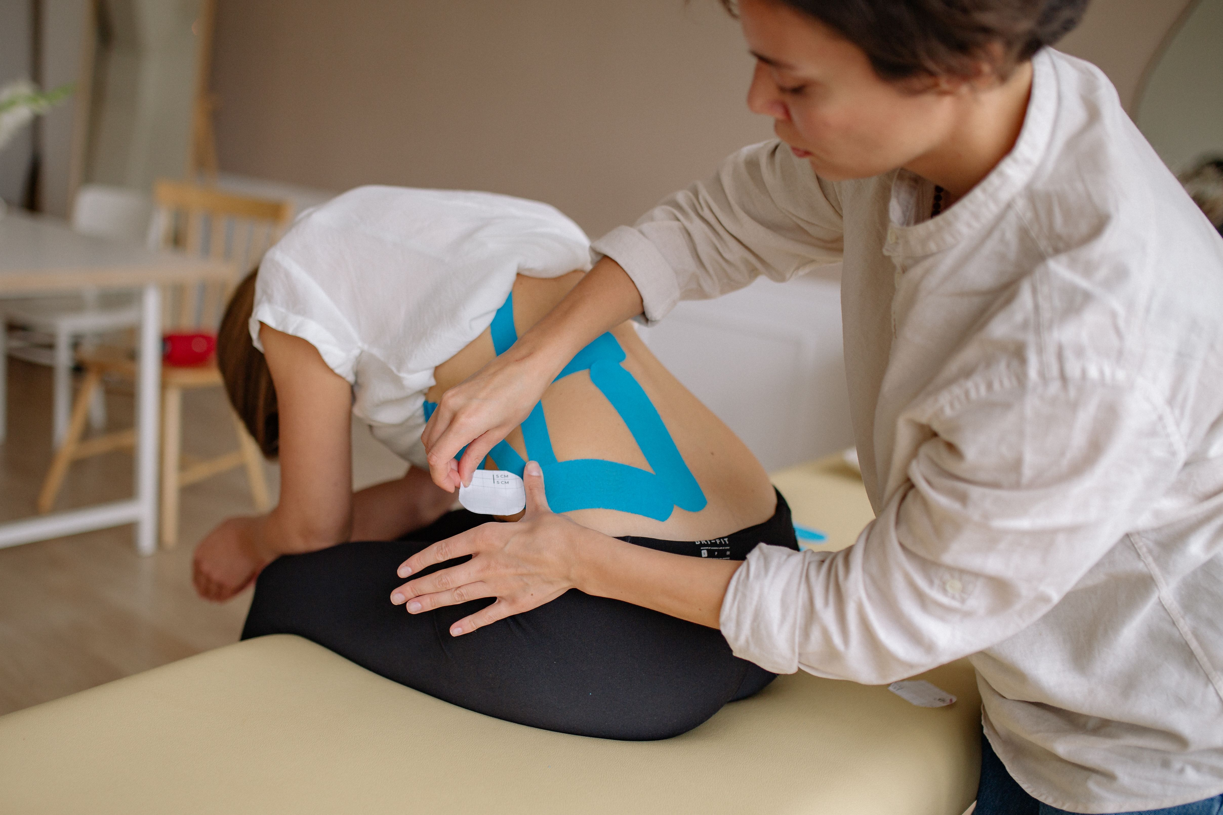 Therapist applying kinesiology tape to a patient's lower back during treatment