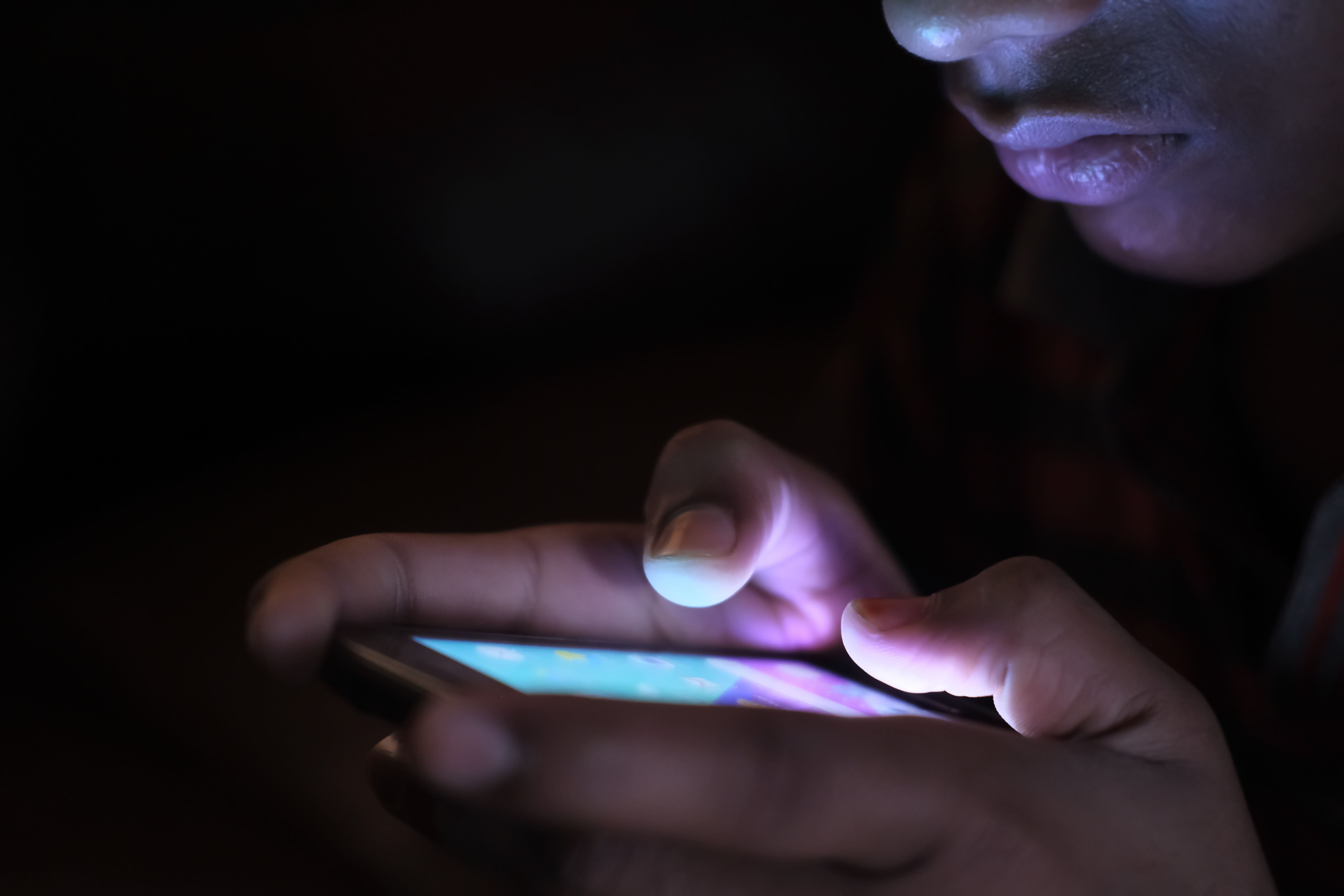 Close-up of a person holding a glowing smartphone in a dark room, playing an online crash game