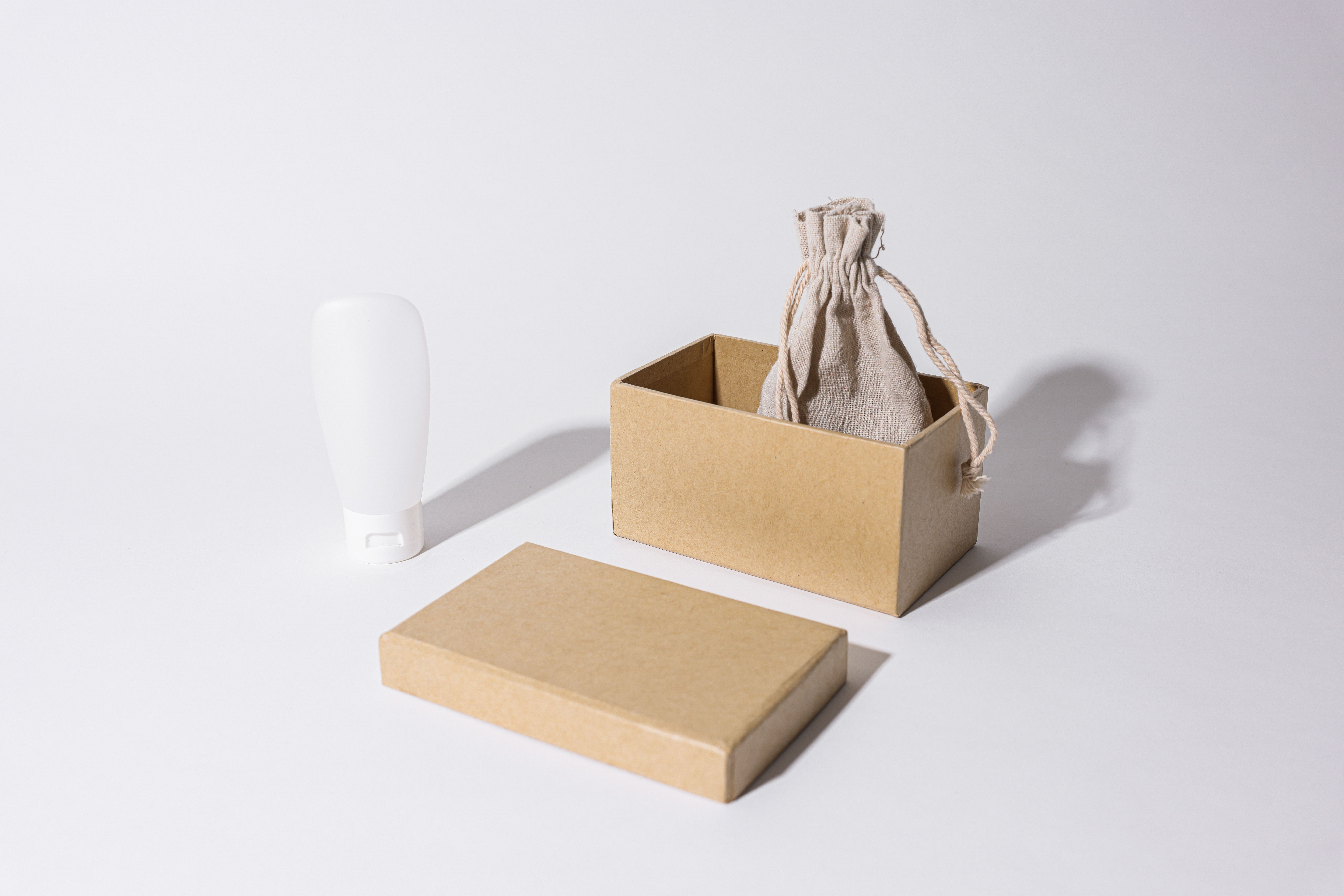 Minimalist mockup of custom packaging with a cardboard box, linen pouch and cream tube on white