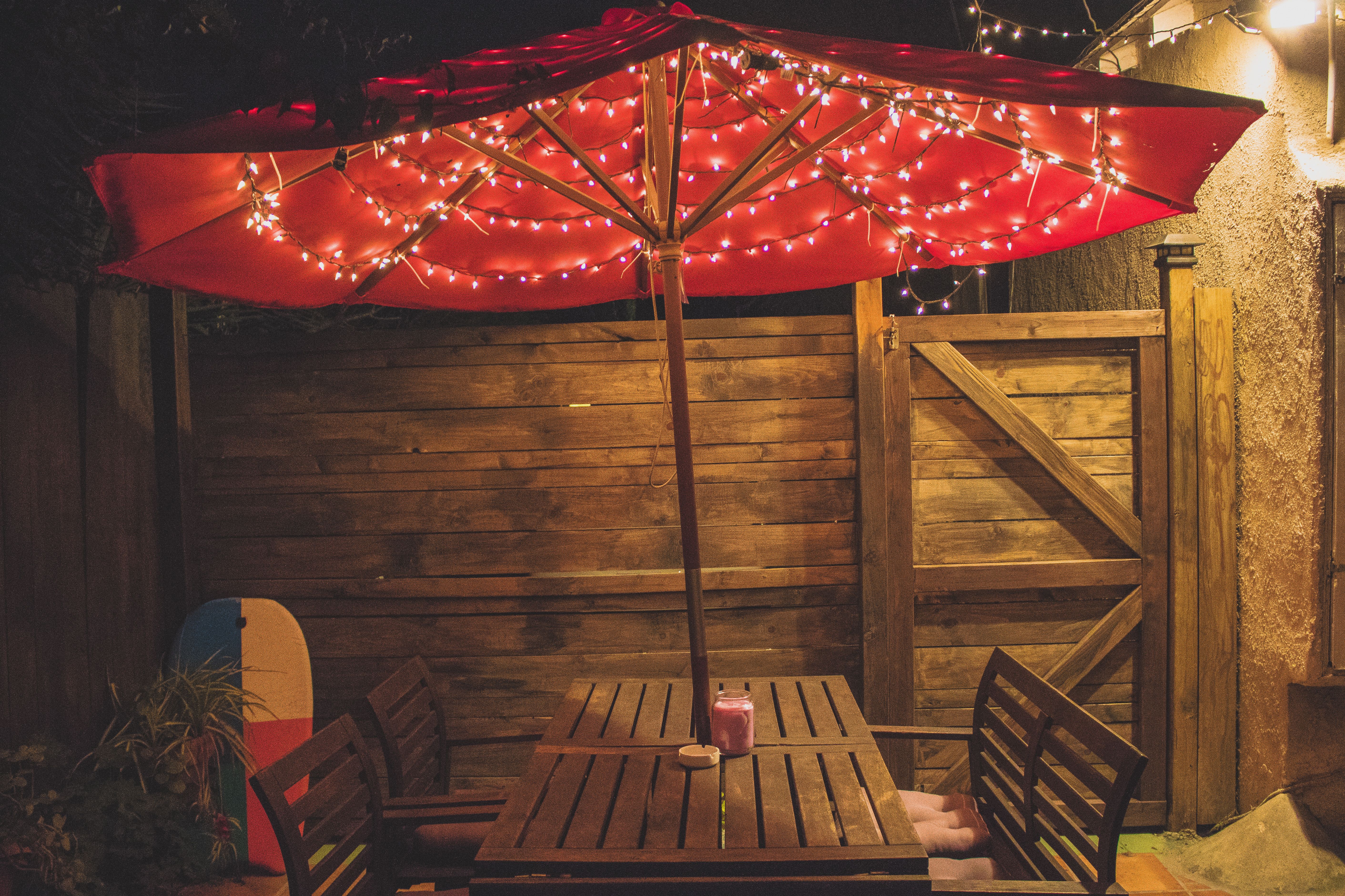 Outdoor dining area with a red parasol and string lights prepared for an evening gathering.