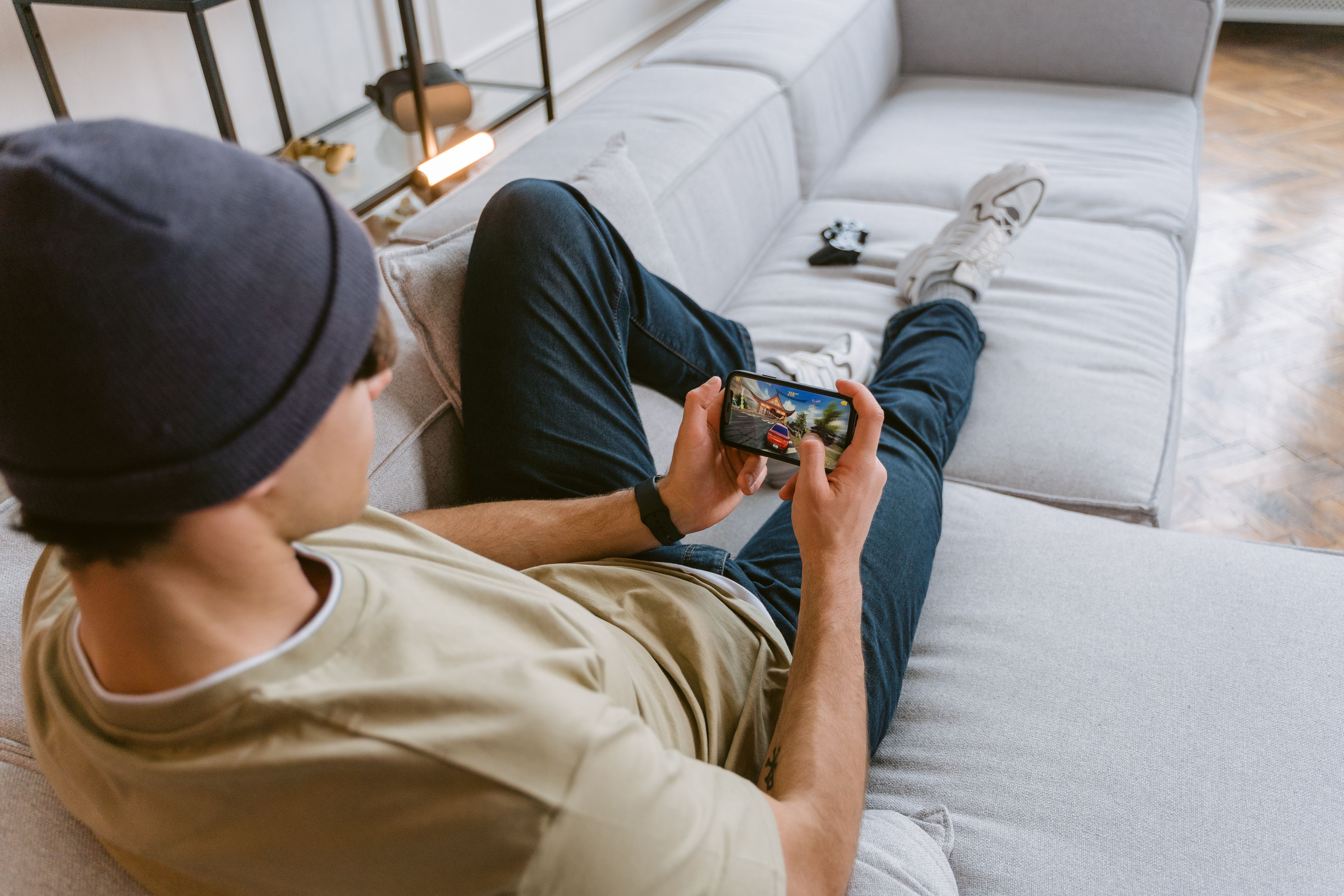 Man casually playing a mobile game on a smartphone from his sofa, illustrating a relaxed mobile casino experience.