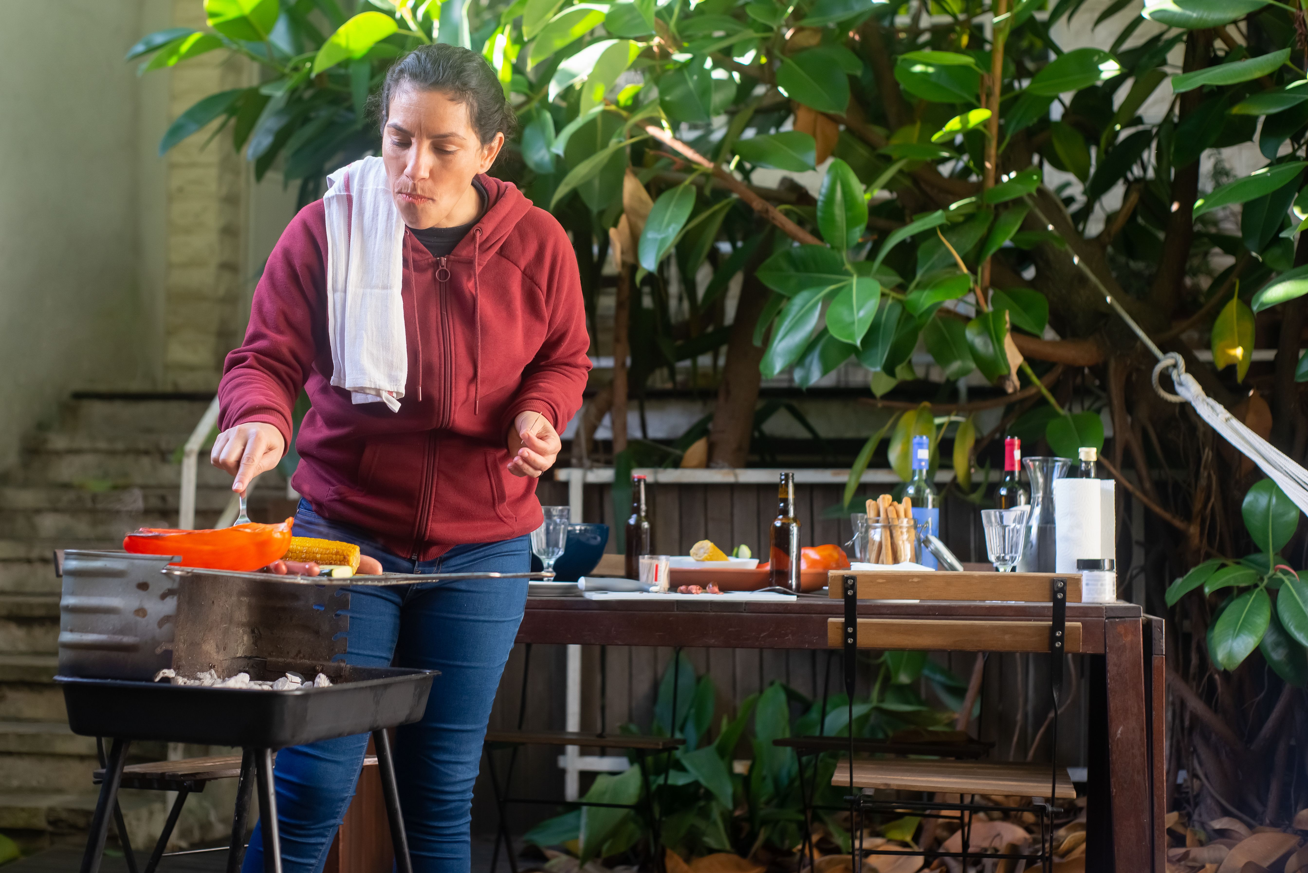 Woman grilling food in an outdoor kitchen surrounded by plants.